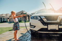 可爱的学龄前小白种女孩洗车在前屋在阳光明媚的夏日。孩子家出差勤务责任理念。玩软管喷水的孩子.
