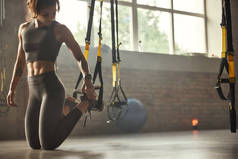 年轻的运动妇女运动服装调整trx健身带，而在健身房训练.