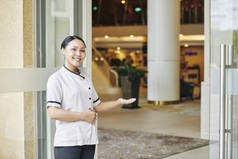 亚洲年轻女子穿着制服站在入口附近，邀请你到酒店