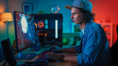 专业玩家玩第一人称射击在线视频游戏在他的强大的个人计算机与五颜六色的霓虹灯。年轻人戴着帽子。客厅用暖灯照明。晚上.
