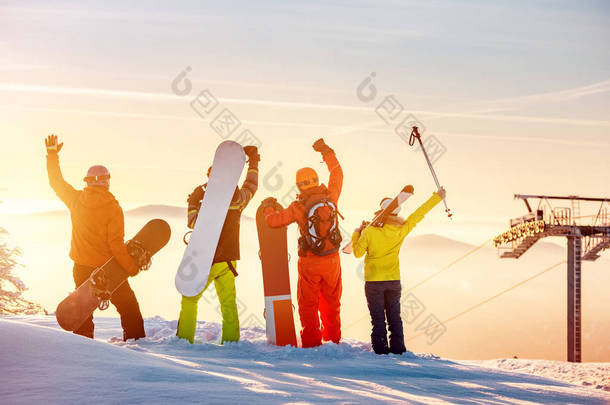 Happy skiers and snowboarders at sunset mountain top