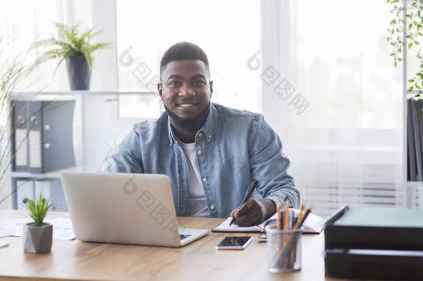 在新工作场所做笔记的面带微笑的黑人<strong>学员</strong>的画像
