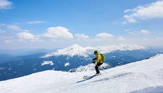 身穿头盔和护目镜的运动员，背着背包沿着陡峭的雪坡滑行，背景是蓝天和美丽的山景