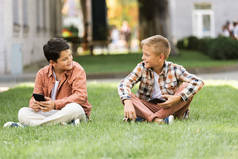 两个笑着的兄弟一边坐在草坪上一边用智能手机聊天