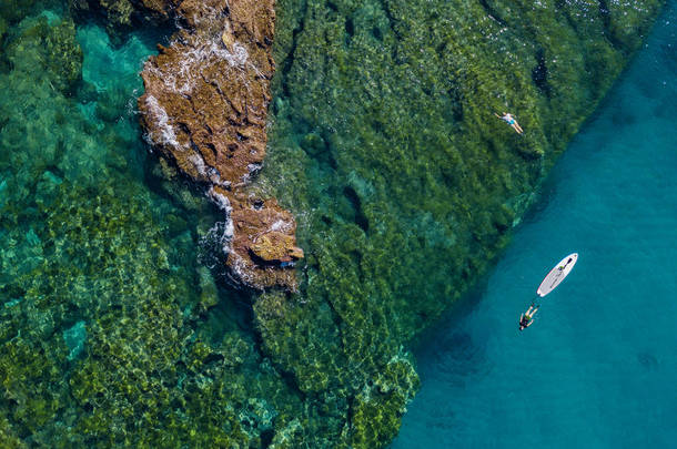 在空中看到水面上有一块桨板漂浮在透明的海面上，在浮潜。 在海上洗澡。 意大利卡拉布里亚Tropea 。 潜水、放松和暑假。 意大利海岸、海滩和岩石.