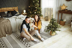 这对快乐的夫妇和一条狗坐在床边，圣诞节。 在家里过新年。 家庭和日期