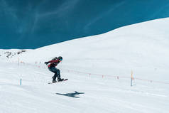 2019年3月10日。 Saalbach，奥地利。 自由式滑雪板滑行在积雪覆盖的斜坡上，在蓝天上留下雪粉