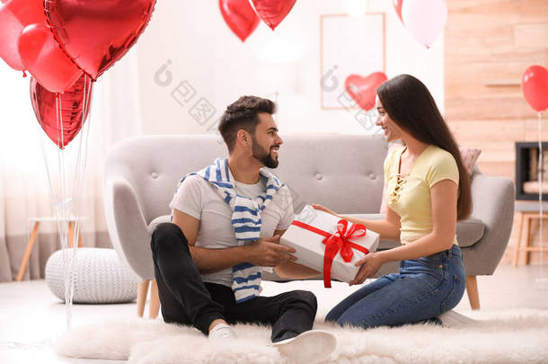 可爱的年轻夫妇，客厅里有礼品盒，装饰有心形气球。 情人节庆祝活动