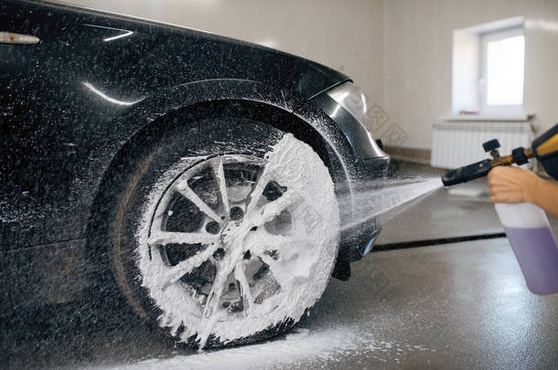Female washer applies foam to the wheel, car wash. Woman cleans vehicle, carwash station, car-wash b