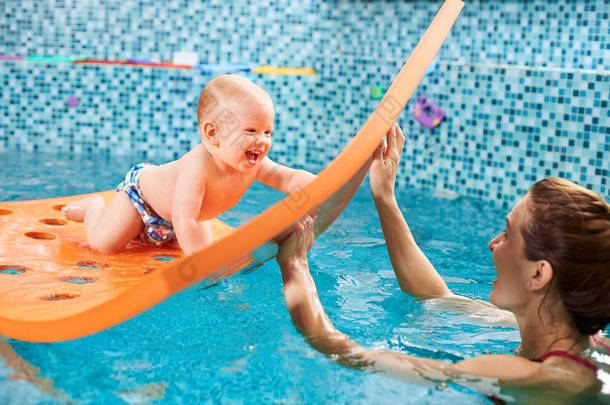 Snapshot of a very <strong>happy</strong> and playful swimming class with instructor. Cheerful baby boy is crawling o