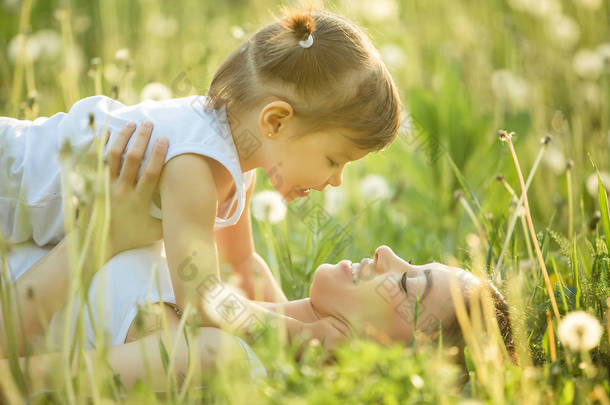 带着春天背景的快乐妈妈和她的小孩的画像。蒲公英田里快乐的一家人。妈妈和她可爱的女儿在外面.
