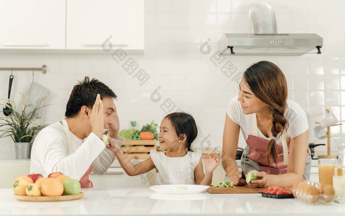 健康的食物在家里,快乐的家庭在厨房概念.母亲和女儿正在吃早饭。可爱的小女孩和她美丽的父母在厨房做饭时正在做早餐.