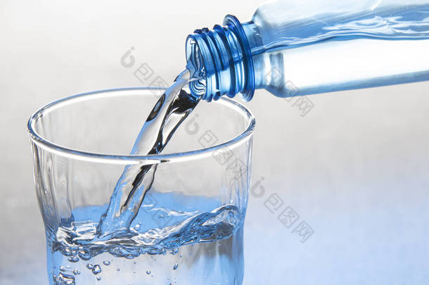 水从瓶子里<strong>倒入</strong>一只玻璃<strong>杯中</strong>，杯子被白色的底座隔开了
