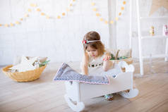 穿着白色连衣裙的可爱小女孩在一间明亮的儿童房的洋娃娃床上玩耍，房间里装饰着玩具和花环.