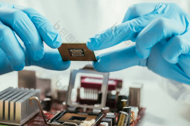 在计算机主板附近持有微型芯片的工程师的部分视图