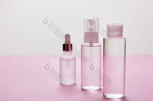 <strong>粉色</strong>和灰色背景的喷雾、<strong>化妆品</strong>瓶和装有液体的血清瓶  