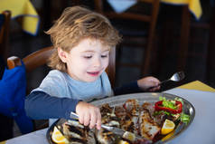 快乐的男孩在餐馆里用刀叉吃鱼。行为举止。在咖啡店吃午饭。婴儿和健康食品。学生和午餐。儿童的食欲.