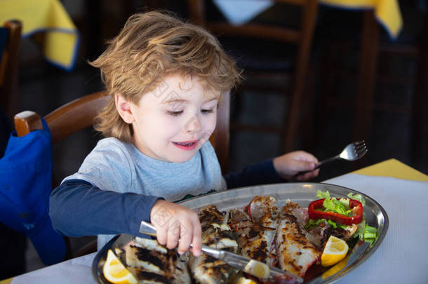 快乐的男孩在餐馆里用刀叉吃鱼。行为举止。在咖啡店吃午饭。<strong>婴儿</strong>和健康<strong>食品</strong>。学生和午餐。儿童的食欲.