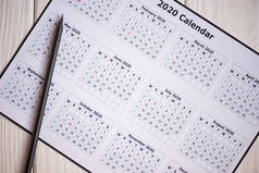 木制背景图上2020年日历和铅笔的顶视图