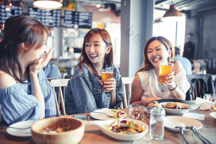 快乐的年轻女子坐在餐厅里享用晚餐和啤酒代餐