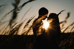 在秋天的日落时分,一对年轻夫妇在公园的户外拥抱和亲吻.在阳光背景下的草地上。友好家庭的概念。上半身靠近点文本和设计的位置.