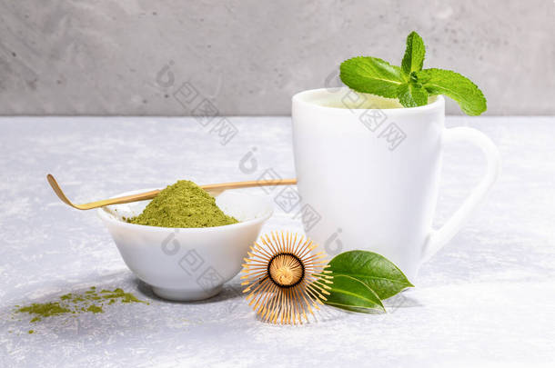 白杯配马沙绿茶，粉配上特殊木制勺子，竹浆，灰色背景下的新鲜叶子. 