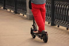 在公园的柏油路上，一名身穿红色长裤的男子骑着电动车在夏天的一天里，近视腰高的后视镜，可供选择的交通工具