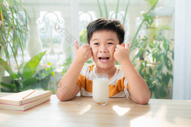一个亚洲男孩做完<strong>作业</strong>坐在桌子边喝牛奶。电子学习和教育概念.