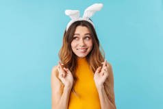 在工作室里，年轻快乐女人的画像，戴着玩具兔子耳朵笑着，手指在蓝色背景下相互交叉