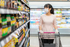 亚洲妇女，戴着卫生面具，戴着橡胶手套，购物车在杂货店里，正在寻找酱汁或调味品，准备在流感大流行期间进行检疫