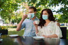 年轻夫妇一起在户外喝茶时戴着面具，带着有趣的考拉威斯流行观念