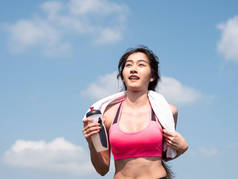 近前视野年轻的亚洲女人在室外阳光下在路上奔跑。女慢跑者在大自然中运动时，手持瓶装水。健康和健康的生活方式