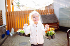 一个金发碧眼的小女孩带着两包玛丽戈尔德呆在她的后院。这个女孩要去移植花。家庭园艺
