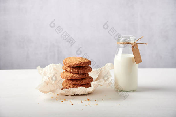 <strong>浅褐色</strong>烘焙纸上堆放的饼干，旁边的奶瓶，白色木制桌子上有标签，背景<strong>浅</strong>灰色，有很多负面的空间，侧面看
