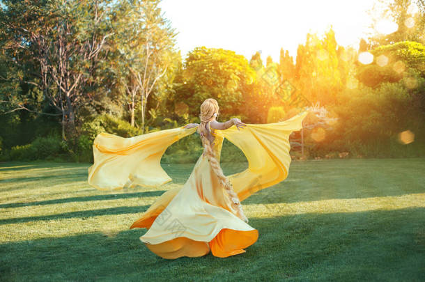 明亮的神圣阳光。艺术幻想快乐的女人手舞着升起黄色丝绸裙，斗篷火车在风中飞舞。金发姑娘长发辫子.长发公主后视镜
