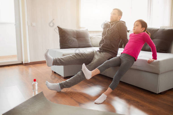 父亲和女儿正在家里接受训练。在公寓里锻炼。运动在家里。在家里的地板上，有腿抬高的板