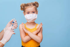 医生给一个戴口罩的金发小女孩注射疫苗. 