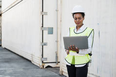 在集装箱货港工作的黑人工头拿着手提电脑检查集装箱。非洲码头女职员业务物流进口航运概念.