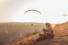 一对恋爱中的年轻夫妇正坐在山坡上，沐浴在夕阳西下的阳光中，女孩把施瑙策抱在怀里。他们拥抱，看着空中飘扬的滑翔伞。软焦点的照片