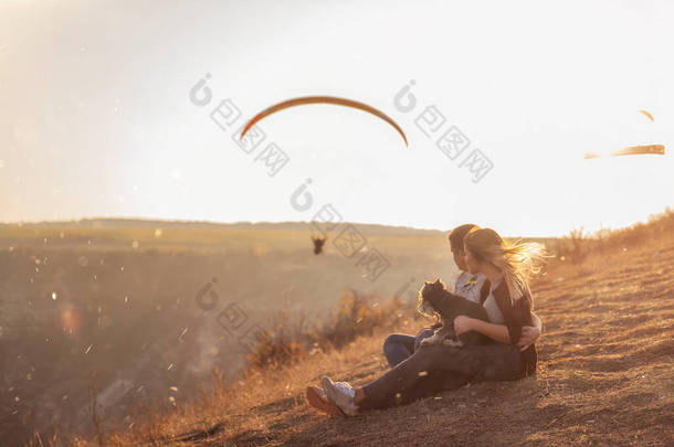 一对恋爱<strong>中</strong>的年轻夫妇正坐在山坡上，沐浴在夕阳西下的<strong>阳光中</strong>，女孩把施瑙策抱在怀里。他们拥抱，看着空<strong>中</strong>飘扬的滑翔伞。软焦点的照片