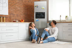一对快乐的夫妇坐在厨房冰箱旁边的地板上