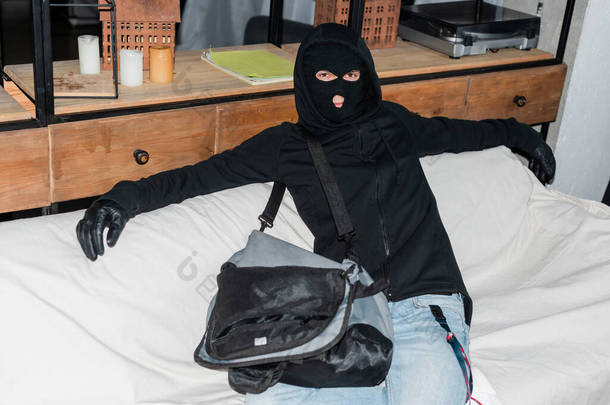 穿着巴拉克拉瓦的强盗坐在手提电脑旁，坐在手提包里看着相机 