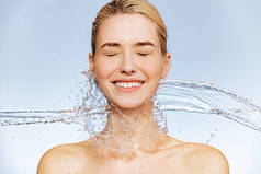 照片上的年轻女子皮肤洁白，水花斑斑。一个笑容满面的女人的画像。温泉治疗。女孩用水洗她的身体。水和身体.