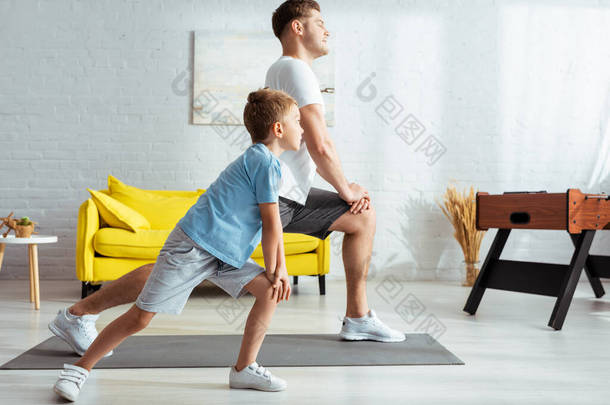 年轻的父亲和可爱的儿子在家里锻炼的时候做突然运动的侧视图
