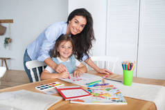 微笑着母亲和女儿准备上课，并用铅笔和颜料在桌边画画。学前教育的父母和学生。秋天的第一天。小班的女生，回学校.