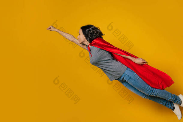 我在飞！一个全长的，向左拐了一个年轻姑娘的照片，描绘了一个飞行中的超级女主人公，这是一个经典的超级英雄的姿势，穿得很随便，但穿着红色的超级英雄飘逸的斗篷.