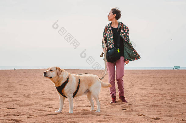 一个女孩<strong>和</strong>一只<strong>小鹿</strong>拉布拉多猎犬在沙滩上散步。带着一只狗在海上旅行
