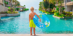 小男孩站在游泳池边，手里拿着一个蓝色和黄色的游泳池。暑假、旅游、旅游、度假等概念.旅馆业复制空间横幅.