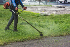 一个人雨后在城市街道上用割草机割草。夏天的城市生活.