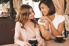 两个年轻美丽的嬉皮士女孩穿着时髦的夏装。无忧无虑的女人在阳台上聊天和喝咖啡。积极的模特们在一起玩乐和交流